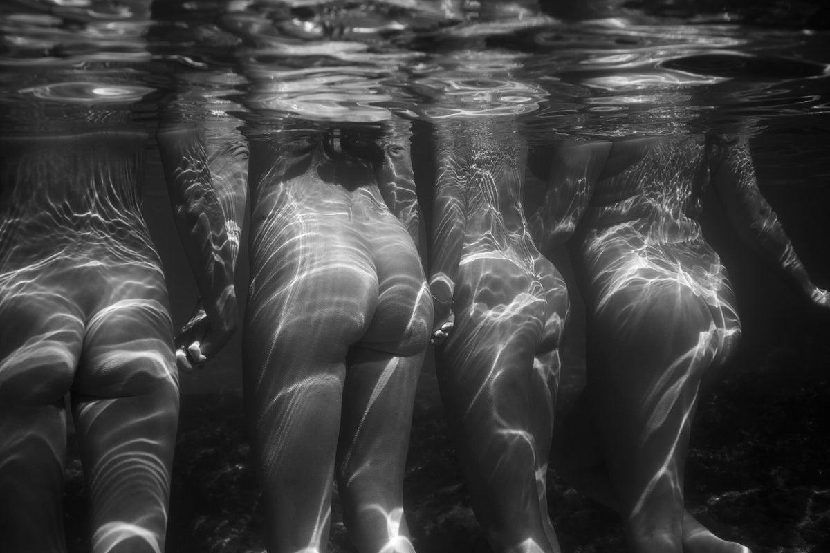 United We Stand – black and white underwater fine art photograph of multiple female figures standing side by side, legs submerged, light refracting across their forms, by Emma Maggs